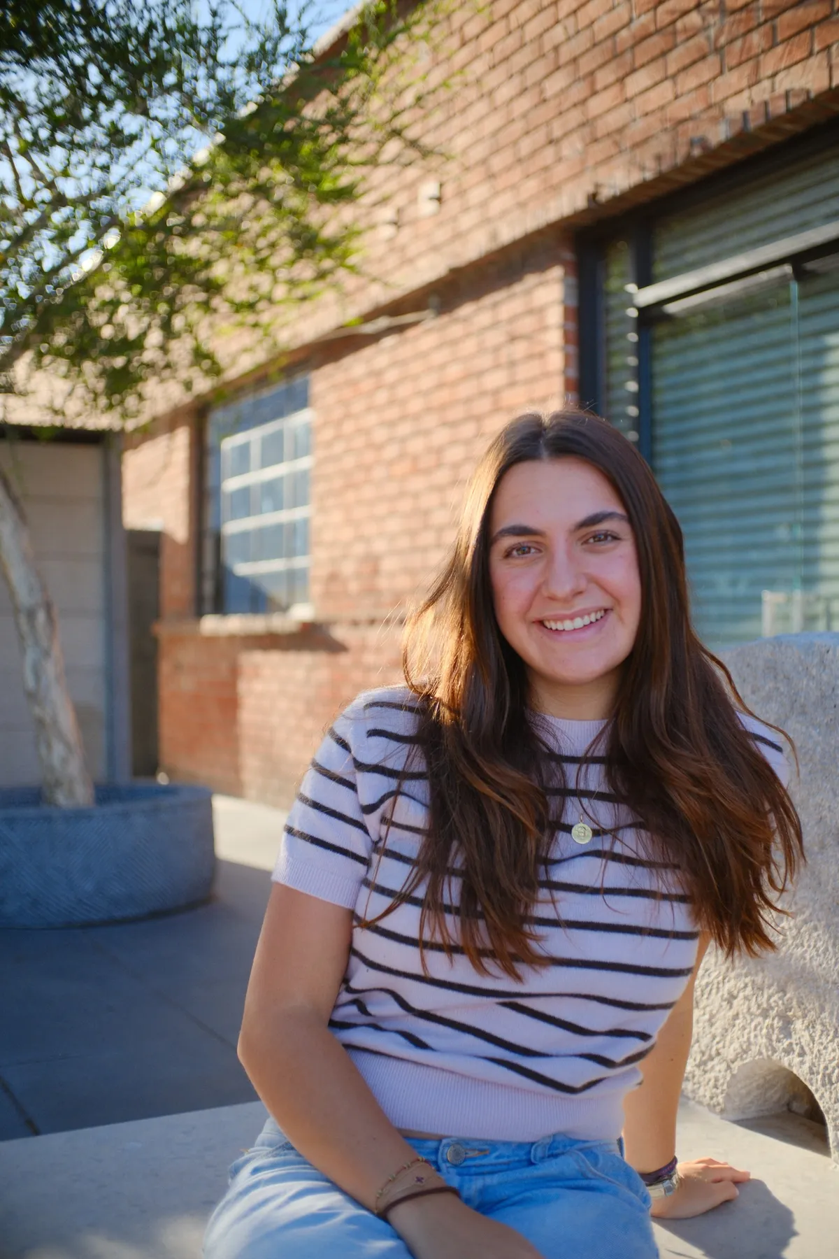 Daniella Raphael seated outside against a brick wall